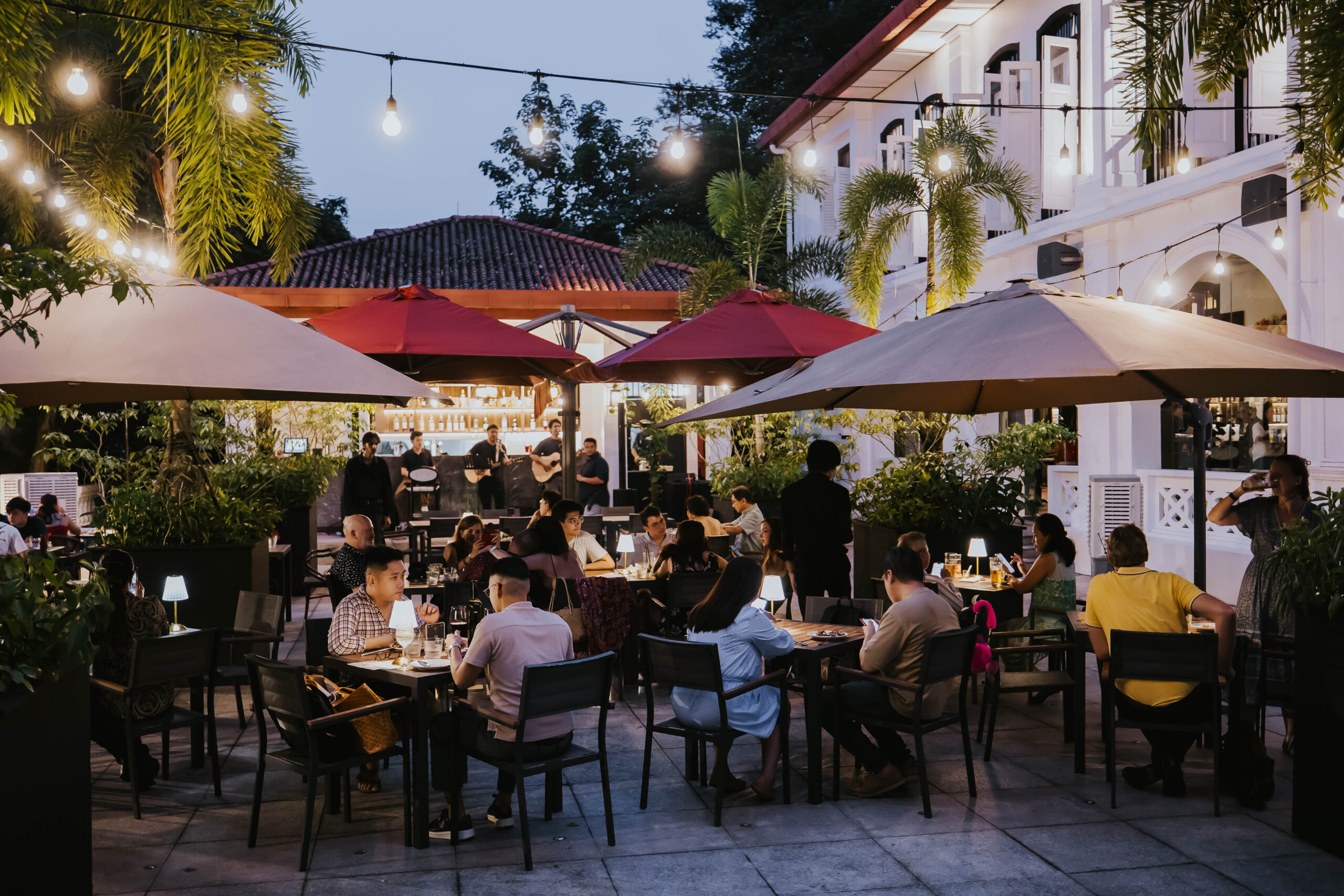 Guests dining under umbrellas and string lights on the terrace at The Alkaff Mansion, 1918 Heritage Bar Singapore