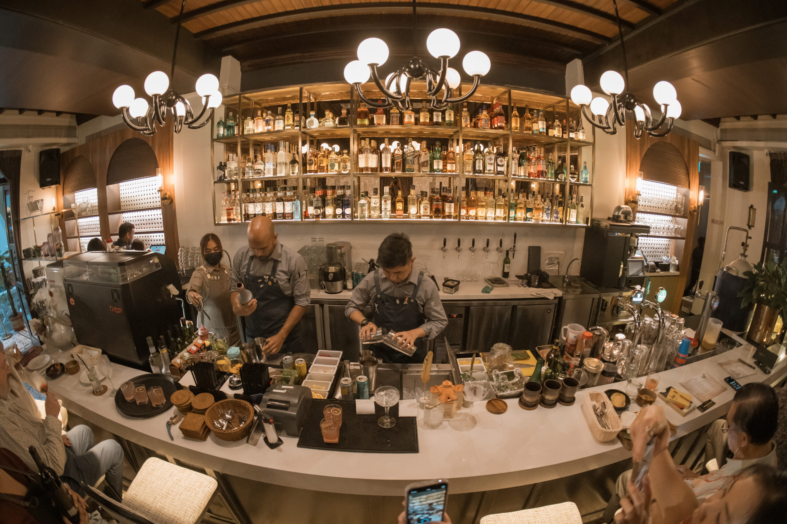 Bartenders crafting cocktails at the 1918 Heritage Bar counter with chandeliers and back bar, The Alkaff Mansion Singapore